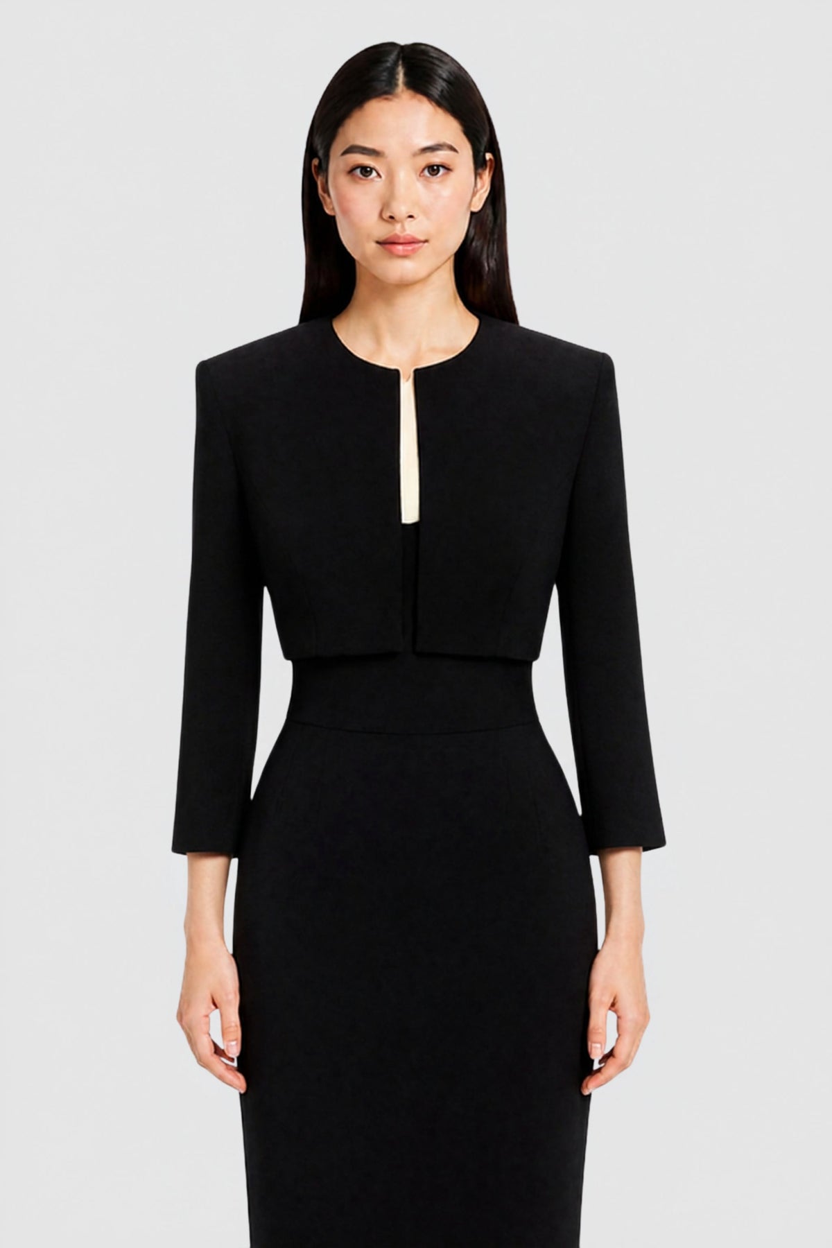 A woman modeling a black two-piece silk evening set consisting of a cropped long-sleeve jacket and matching dress