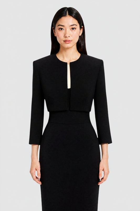 A woman modeling a black two-piece silk evening set consisting of a cropped long-sleeve jacket and matching dress